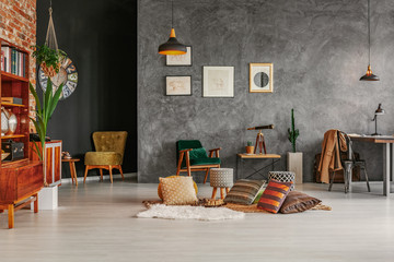 Patterned cushions on the floor in grey workspace interior with posters and chair at desk. Real photo