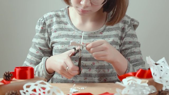 Girl teenager with glasses carving snowflakes out of paper. Concept preparation for the New year.