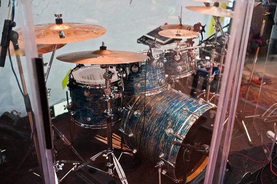 Drum set on stage in a concert hall behing glass wall.