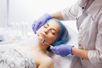 Fototapeta premium Cosmetology. Beautiful Woman At Spa Clinic Receiving Stimulating Electric Facial Treatment From Therapist. Closeup Of Young Female Face During Microcurrent Therapy.