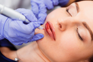 Young woman having permanent makeup on lips in beautician salon. Close up - obrazy, fototapety, plakaty