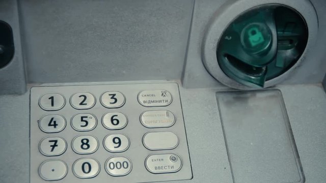 Blinking green slot in gray ATM cash machine. ATM machine is blinking and ready to accept credit card. Metal keypad with digits for pin enter. Green plastic insert. Protection from hackers.