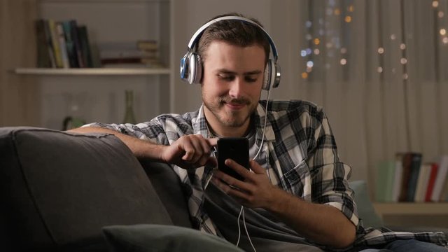 Happy man relaxing on a couch listening to music in the night at home
