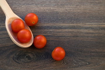 red cherry tomatoes lie on a light wooden spoon and a dark wooden backgraund