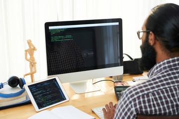 IT technician sitting by workplace in front of computer screen, analyzing data or creating new code or language