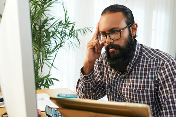 Bearded software developer in casualwear looking at coded data on computer screen and trying to read it