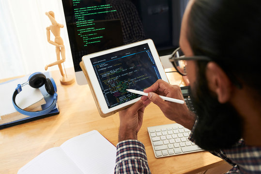 IT developer with stylo pointing at coded data on screen of tablet while scrolling and analyzing it