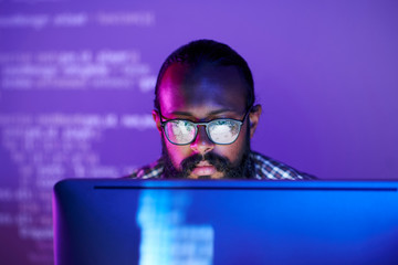 Young serious programmer in eyeglasses concentrating on working with coded data on computer screen - obrazy, fototapety, plakaty