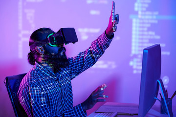 Decoded information reflected from computer monitor on bearded programmer in vr headset sitting in front of it