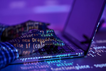 Reflection of electronic data on hands of programmer typing on laptop keypad by desk