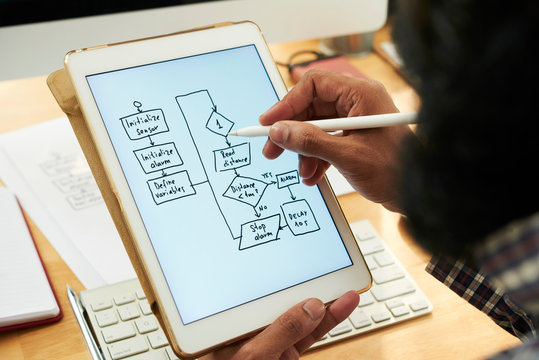 Software developer holding tablet with electronic scheme on display while learning information