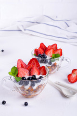 Healthy breakfast in a cup with homemade baked granola, fresh berries, and yogurt on a white table background