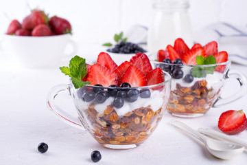 Healthy breakfast in a cup with homemade baked granola, fresh berries, and yogurt on a white table background