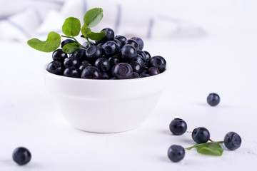 Fresh blueberries with green leaf  in a white bowl on a white background