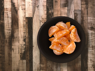 top view of many orange fruits in a black cup on wooden backdrop