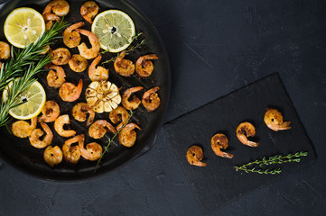 Pan with fried shrimps, fried garlic, rosemary. A stone plaque with shrimp sauce. The view from the top. Black background.