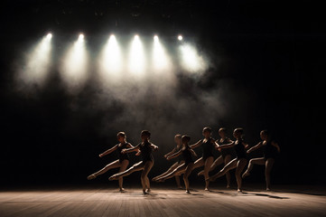 Ballet class on the stage of the theater with light and smoke. Children are engaged in classical exercise on stage.