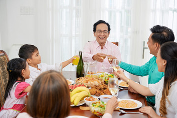 Adult Asian people with children gathering at table at home while toasting with glasses and having celebration