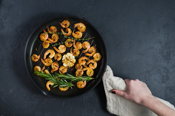 Pan with fried shrimps, fried garlic, rosemary. The view from the top. Black background. Space for text.