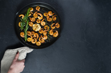 Pan with fried shrimps, fried garlic, rosemary. The view from the top. Black background. Space for text.