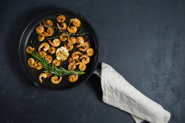 Pan with fried shrimps, fried garlic, rosemary. The view from the top. Black background. Space for text.