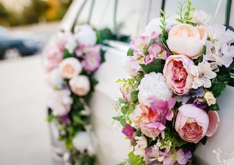 Decorated wedding car. Floral design concept applied to a wedding car. Light violet, soft pink and white roses bouquet hanging on a white car's doors. 