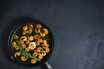 Pan with fried shrimps, fried garlic, rosemary. The view from the top. Black background. Space for text.