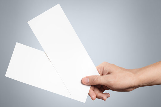 Hand holding two blank sheets of paper (tickets, flyers, invitations, coupons, banknotes, etc.), isolated on grey background