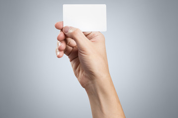 Hand holding a blank card or a ticket/flyer on gray background