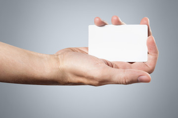 Hand holding a blank card or a ticket/flyer on gray background