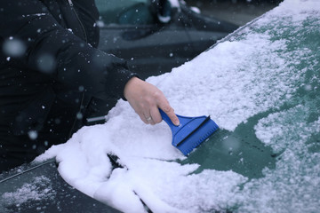 Female driver cleaning snow from windshield