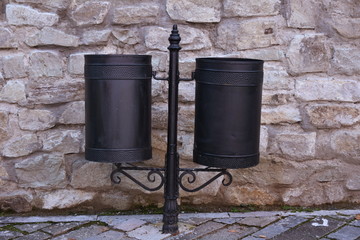 Double  black trash cans (garbage bin) near a stone wall