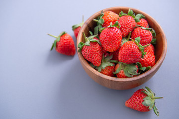 A bowl of beautiful and delicious strawberries isolated on a blue background, closeup, topview, copyspace.
