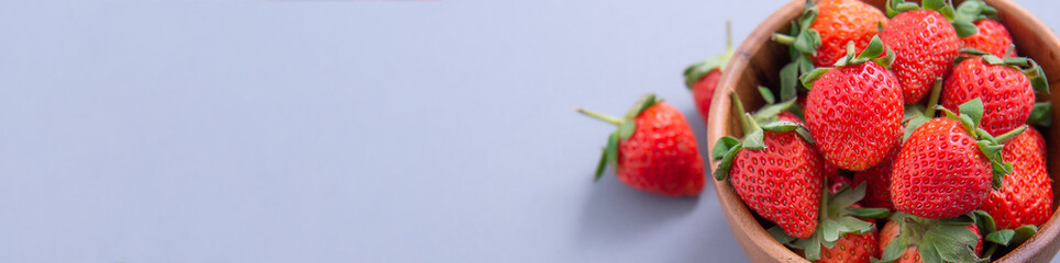 A bowl of beautiful and delicious strawberries isolated on a blue background, closeup, topview, copyspace.