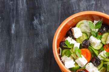 Vegetarian Greek salad with feta cheese, arugula, olives and cherry tomatoes and italian herbs in clay bowl
