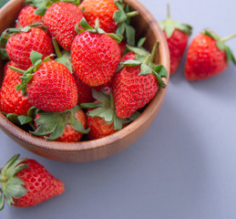 A bowl of beautiful and delicious strawberries isolated on a blue background, closeup, topview, copyspace.