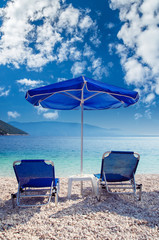 Blue umbrella and tanning beds on the beach. Parasols and sunbeds on a beautiful beach in Greece.