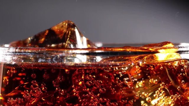 Cola with Ice and bubbles in glass slow motion.