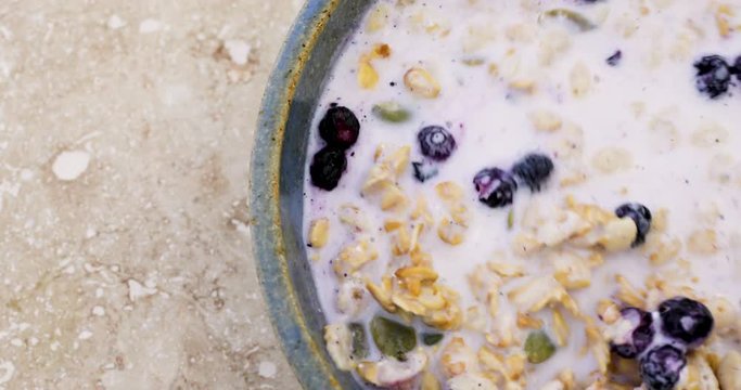 Top close video of stirring organic breakfast cereal with dried blueberries and pumpkin seeds and milk in a bowl then taking a spoonful at the end.