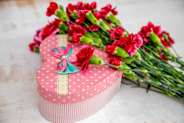  heart-shaped gift box with burgundy carnations lie on a light worn surface,