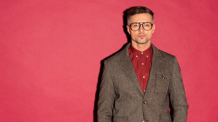 stylish man in glasses and formal wear looking at camera on red background with copy space