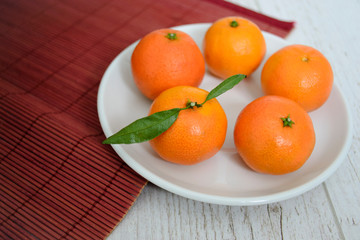 white plate with tangerines on a red straw mat