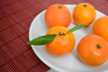 white plate with tangerines on a red straw mat