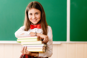 beautiful schoolgirl in red school uniform standing with books in front of the blackboard