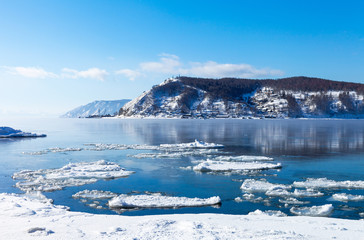 Bank of the Angara River at the source. View of the village of Port Baikal and snow-capped mountains on a sunny day