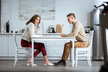 dissatisfied couple sitting with clenched fists at table in kitchen - Powered by Adobe