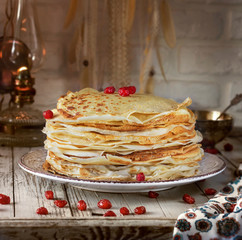 Pancakes with lace edges on a plate. Next cherry berries. In the background kerosene and lace.
