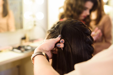Naklejka premium Beautiful girl with long hair, hairdresser weaves a French braid, in a beauty salon. Professional hair care and creating hairstyles.