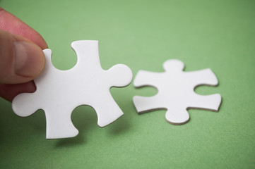 Obraz premium man connecting with hand two jigsaw puzzle pieces on green background. The concept of finding the right solutions in teamwork.