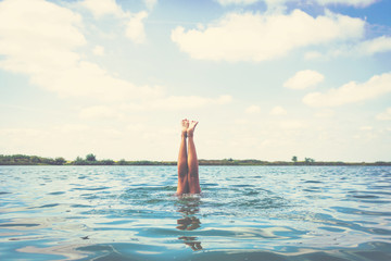Summer feelings. Woman diving into water upside down with legs above surface.